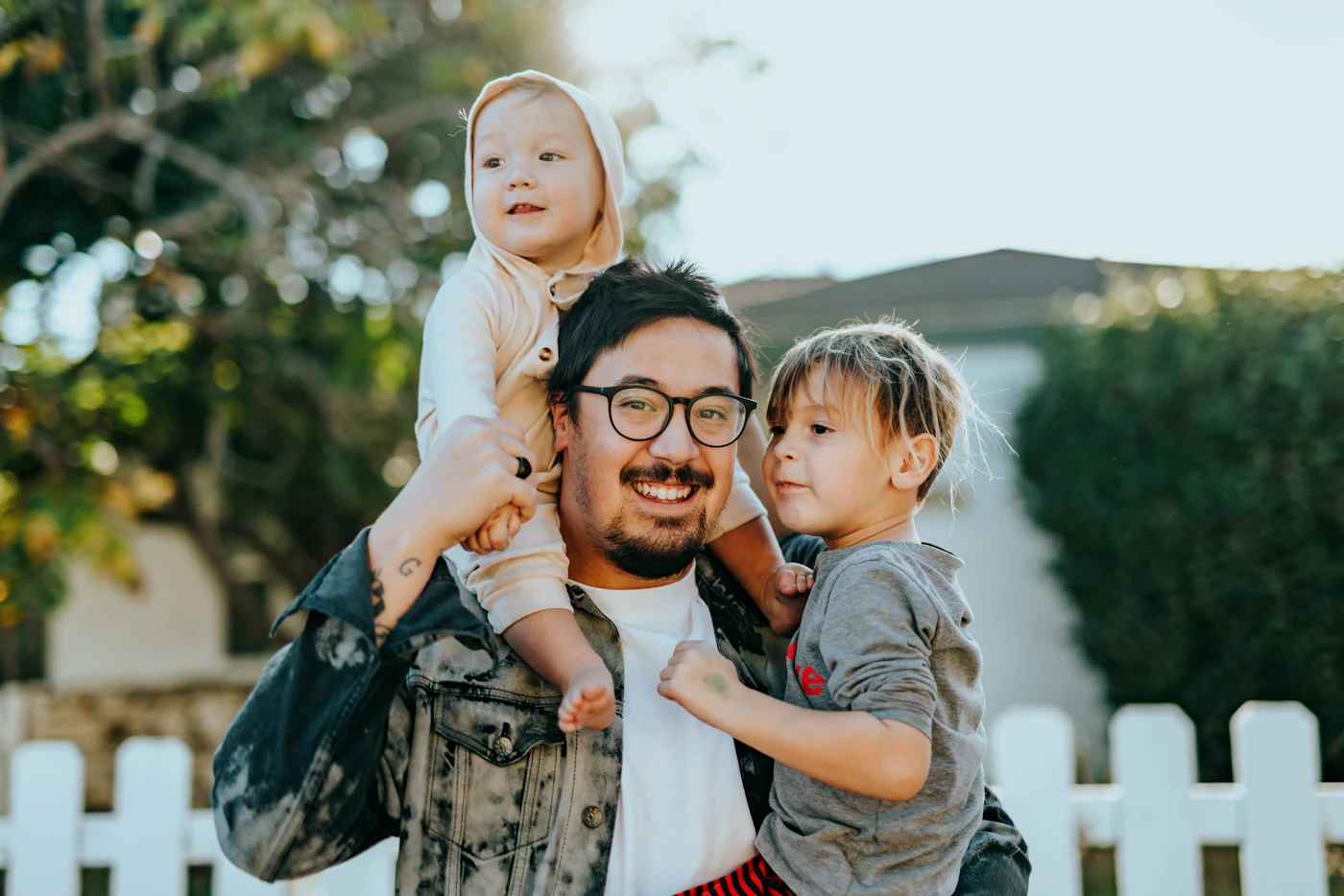 Pai sorrindo carregando os dois filhos pequenos ao ar livre