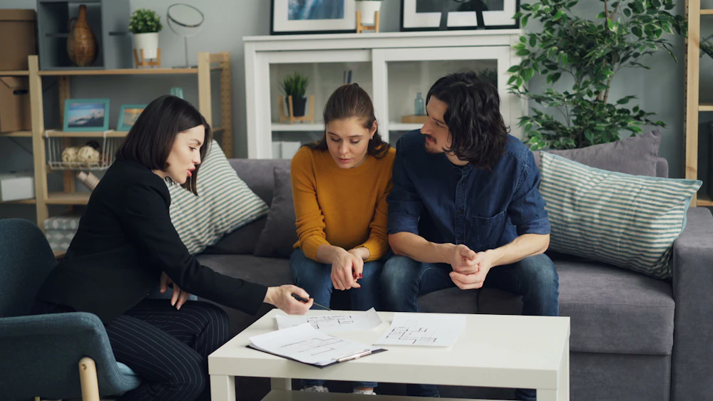Consultora sentada com um casal na sala de casa, conversando sobre documentos na mesa de centro